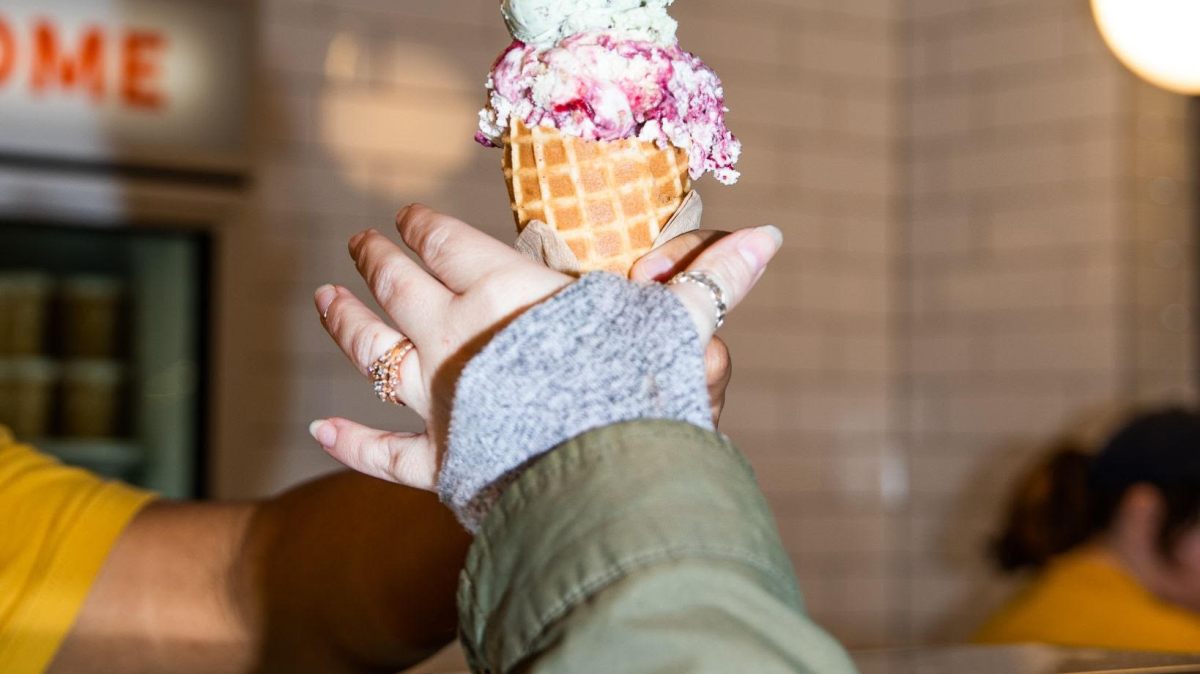 Hand receiving a triple scoop ice cream cone over a counter.
